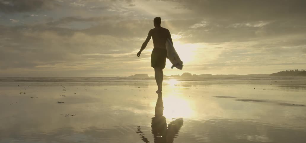 Man carrying a surfboard on a beach at sunset