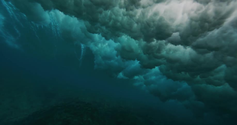 A wave splashes as it rolls overhead and sunlight reflects on the foam underwater