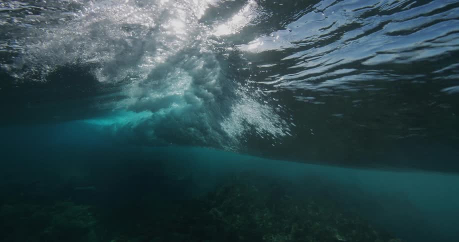 Sunlight peaks through a large wave moving under the surface of the ocean