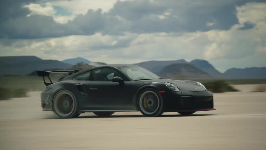 A black sports car driving through the desert driven by a man