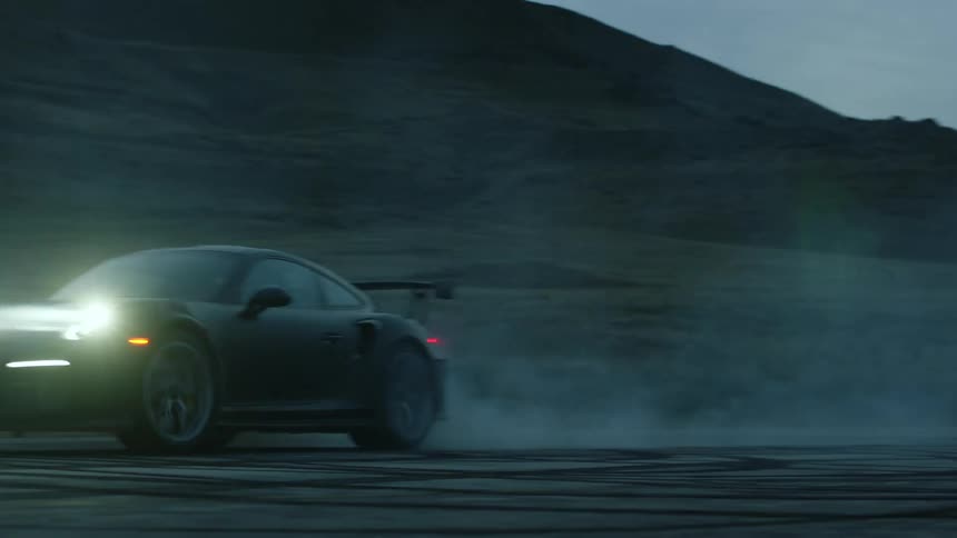 A black sports car burning out on pavement with mountains in the background