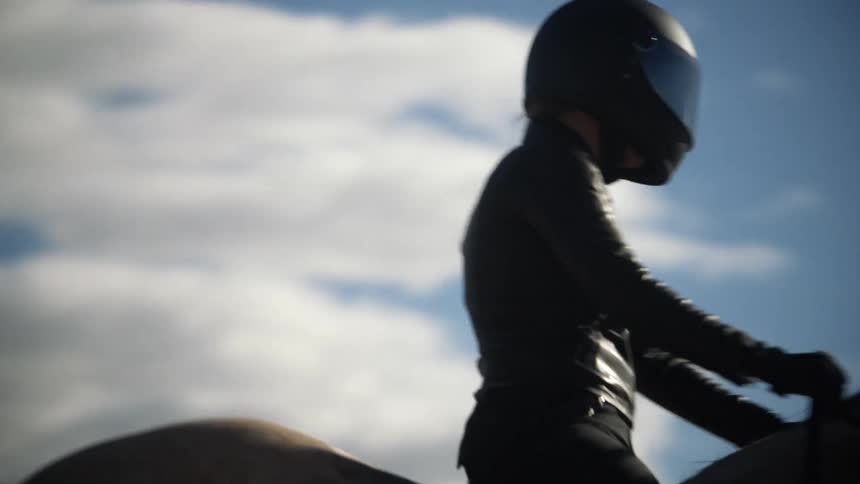 A person wearing black leather and a black helmet riding a horse