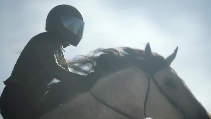 Woman with black helmet leather jacket rides white horse in the desert