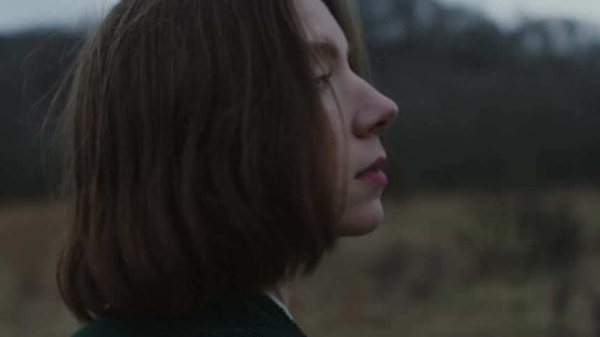 Woman with brown hair and black jacket looks over her shoulder in the field