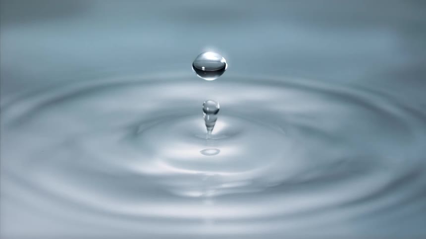 A drop of water splashes onto a smooth liquid surface causing ripples and circles