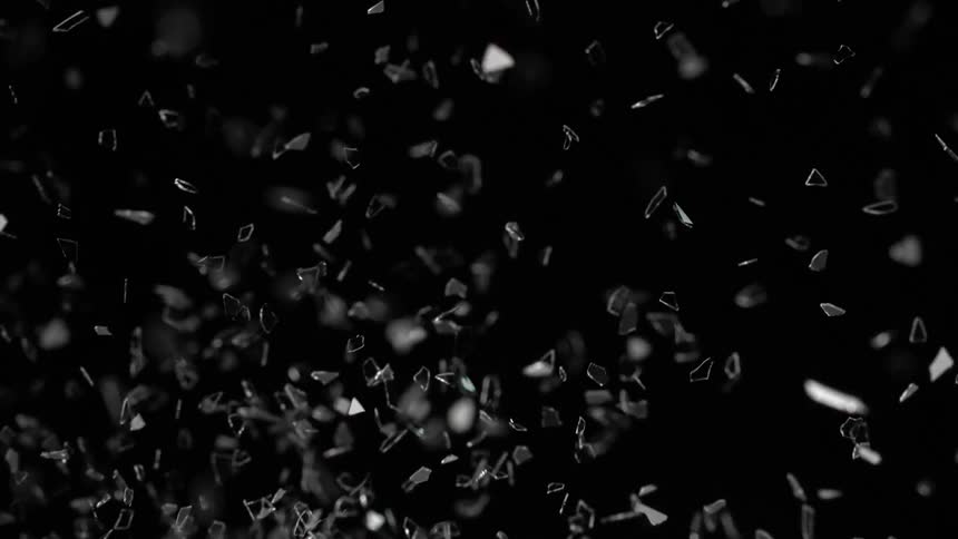 An object is shattering and shards of broken pieces shine and glitter as they fly into the darkness