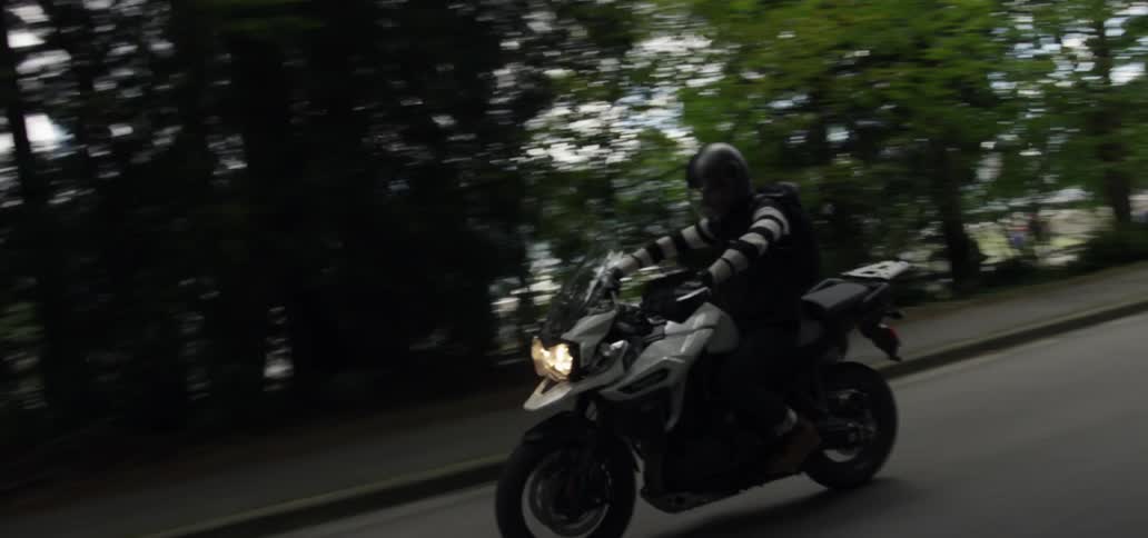 A man riding a motorcycle along a tree-lined urban street