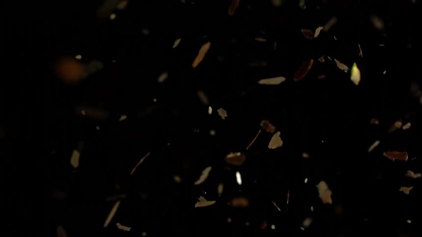 shiny golden flakes reflect light as they fall from above in the darkness