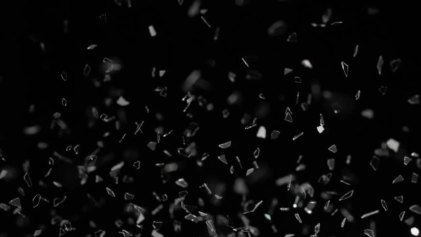Broken pieces of thin glass are thrown into the air on black background