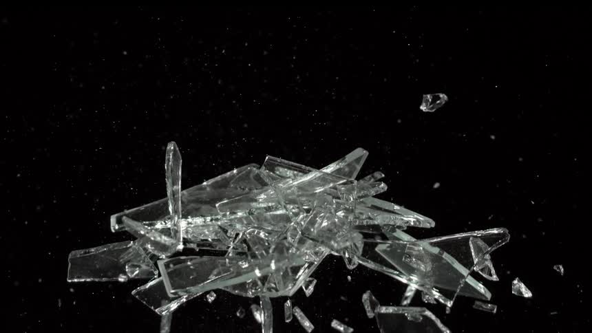 Cluster of glass pieces fly into the air then fall against a dark background