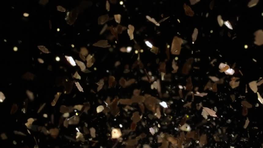 Golden confetti is being thrown into air on black background