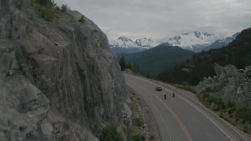 Motorcyclists and cars drive on a mountain road