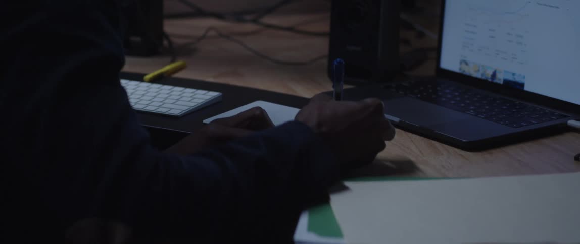 Man with black blazer jacket writes down in notebook sitting at desk in the office