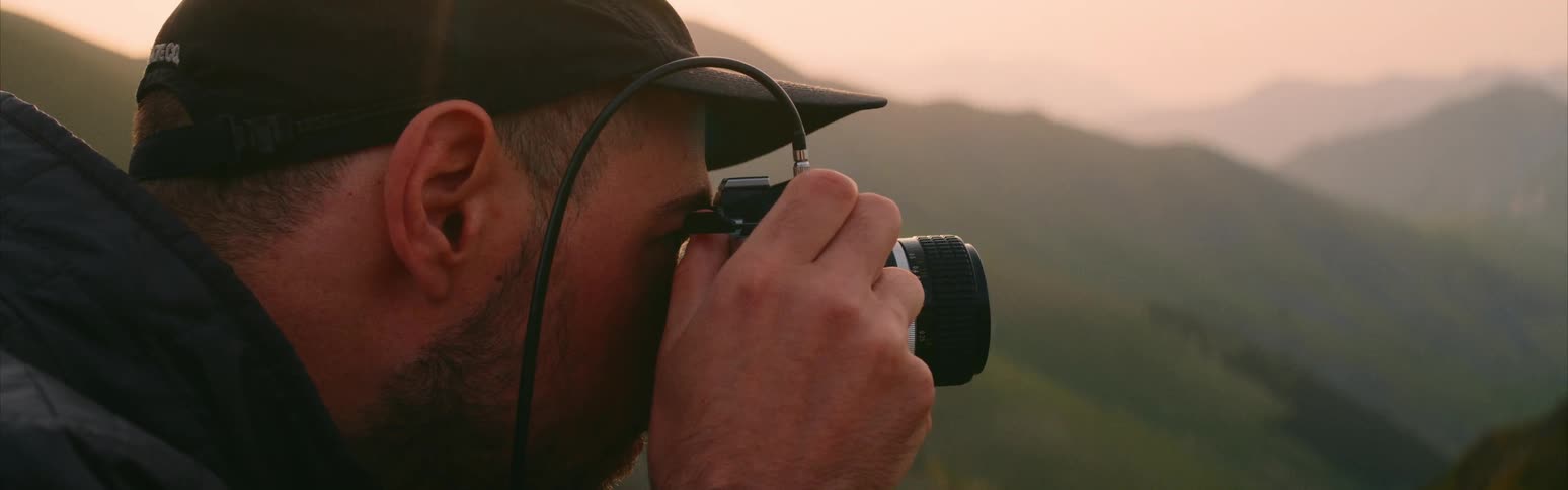Male photographer looks through viewfinder on camera at foggy mountains under a red tinted sky
