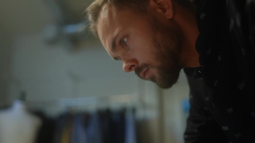 Male tailor with beard and shirt works at tailors shop