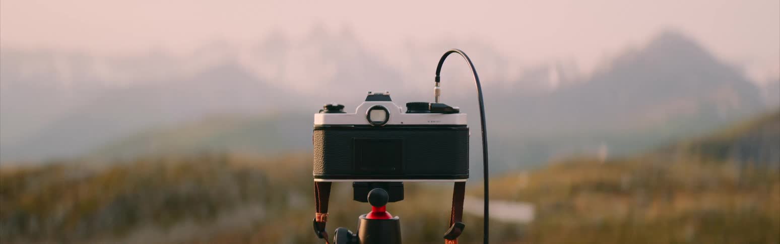 A camera sits on a tripod pointed toward a mountain range