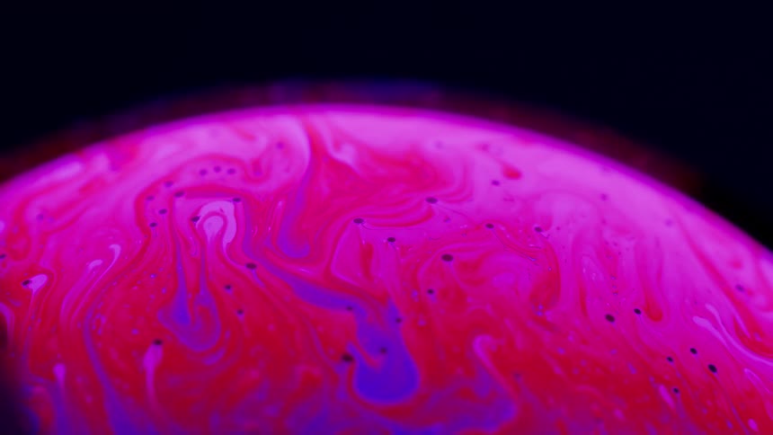 Colorful swirls flow and blend on the curved surface of a bubble against black
