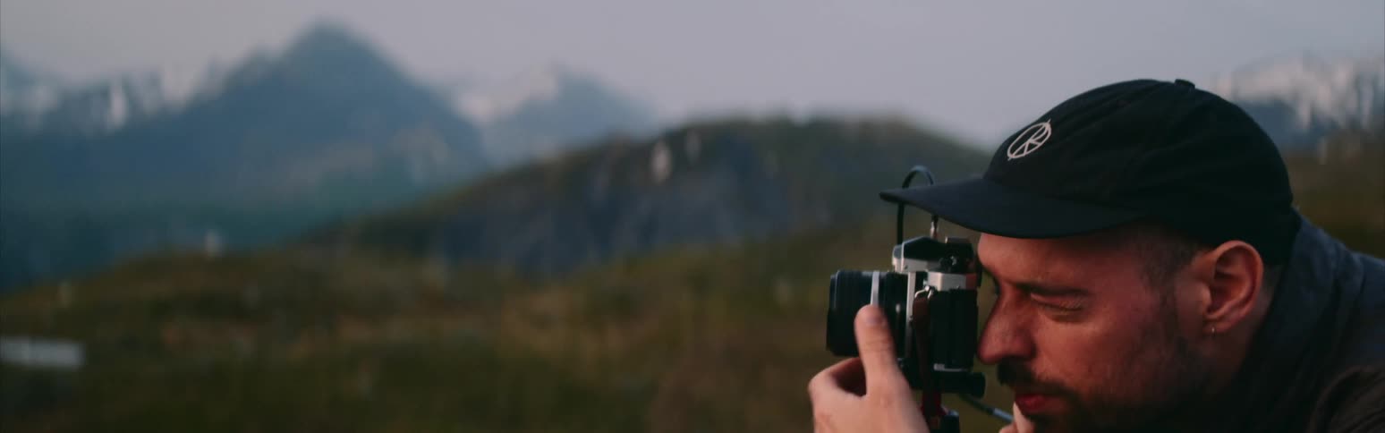 A man squats down squinting to line up a nature shot with a camera on a tripod
