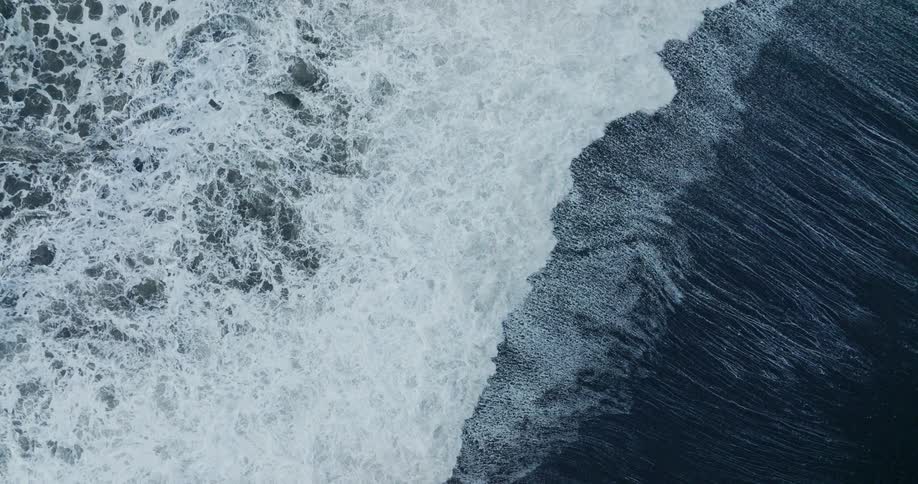 Ocean waves curling breaking and foaming as they came to a black beach shore