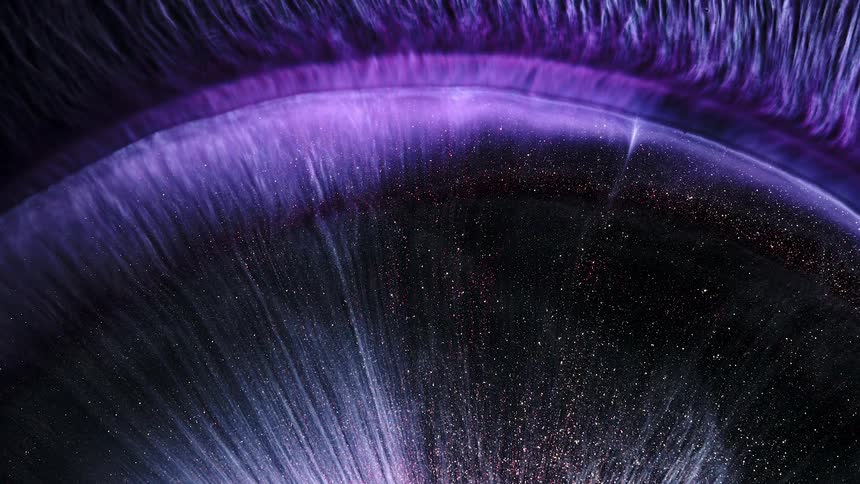 A circle of glitter and color flows and pushes outward in an abstract topography