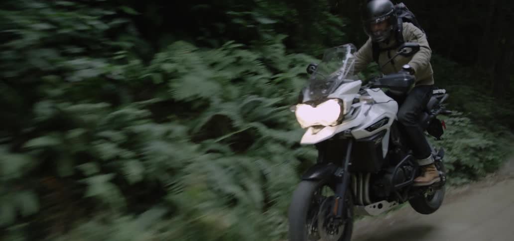 A car following a man on a motorcycle as he drives along a dirt road