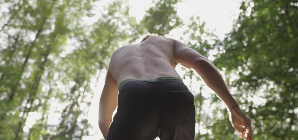 A shirtless man walks in a sunny and forested area