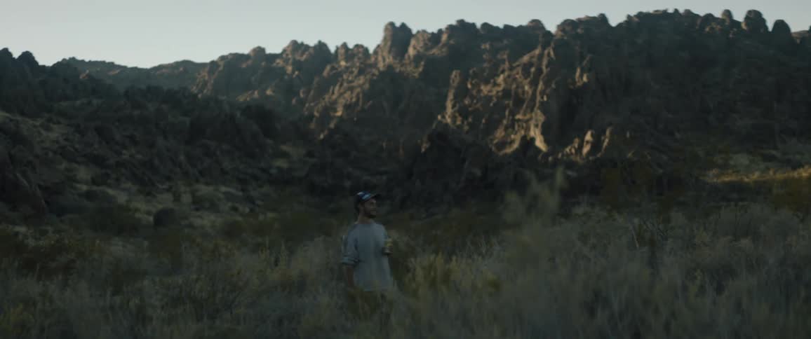 A man holding a beer at the base of a cliff looks around