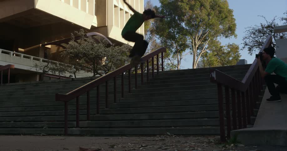 A photographer takes a photo of a teenager while he rides a skateboard down steps