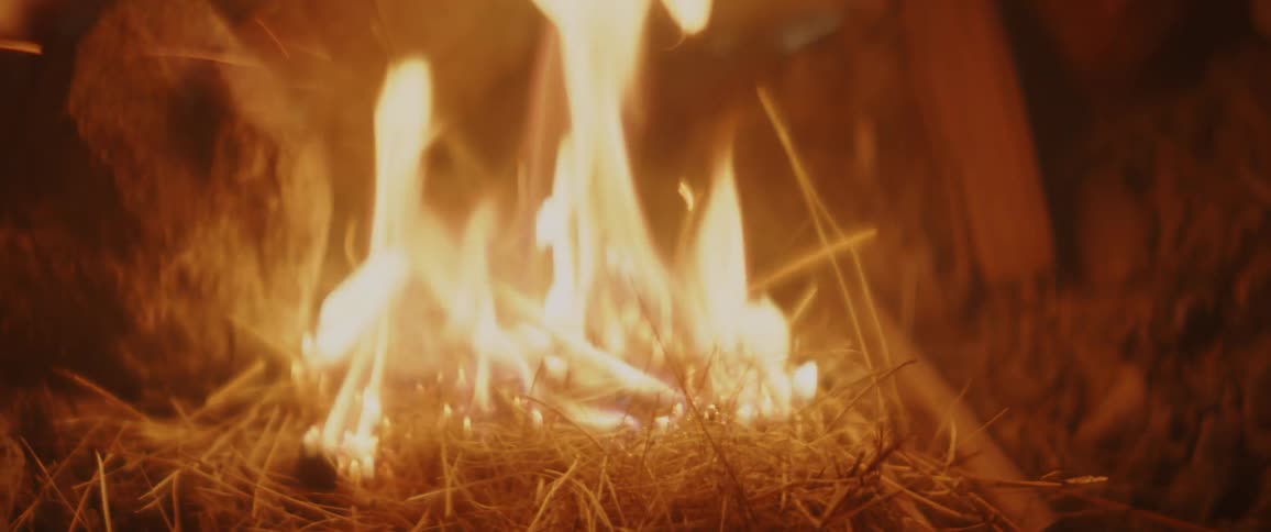 A man uses dried grass and wood chips to build a fire outdoors