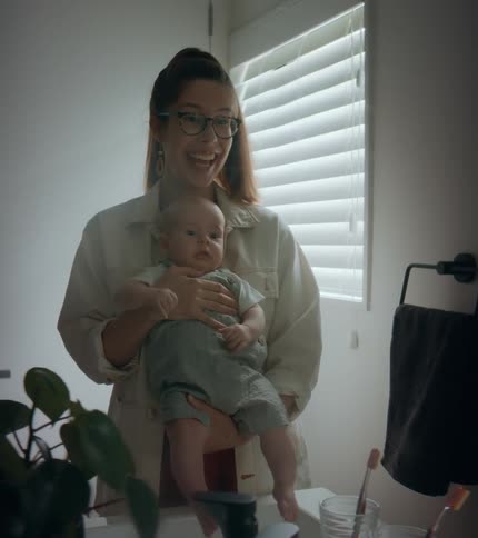 Mother holding baby smiles while showing child their reflection
