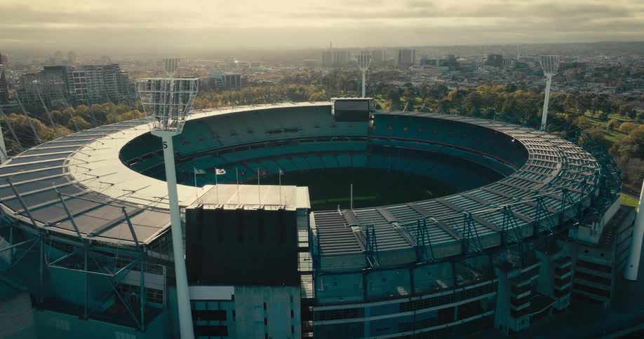 An aerial of a circular stadium surrounded by trees on the outskirts of a city