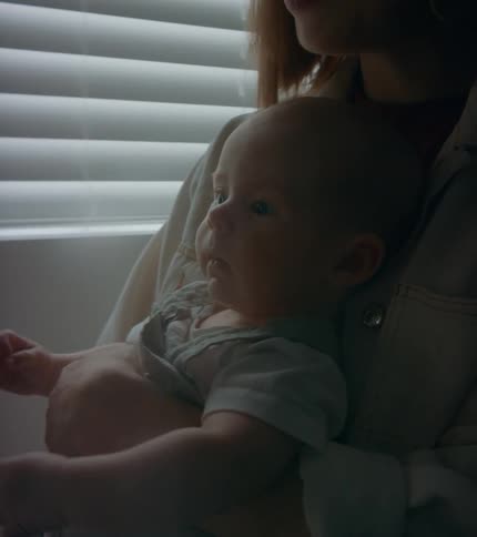 A woman is standing in a room holding her baby who is moving their arms as she talks