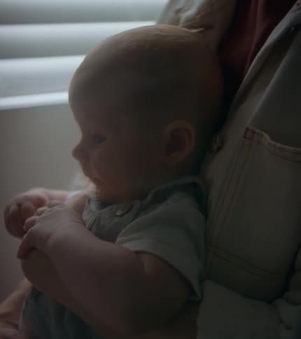 Parent holds baby close near blind covered window