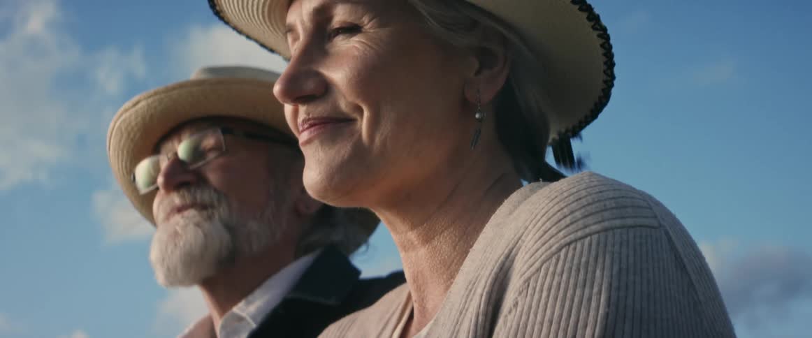 A man and a women wearing similar hats look at each other smiling and then looking into the distance