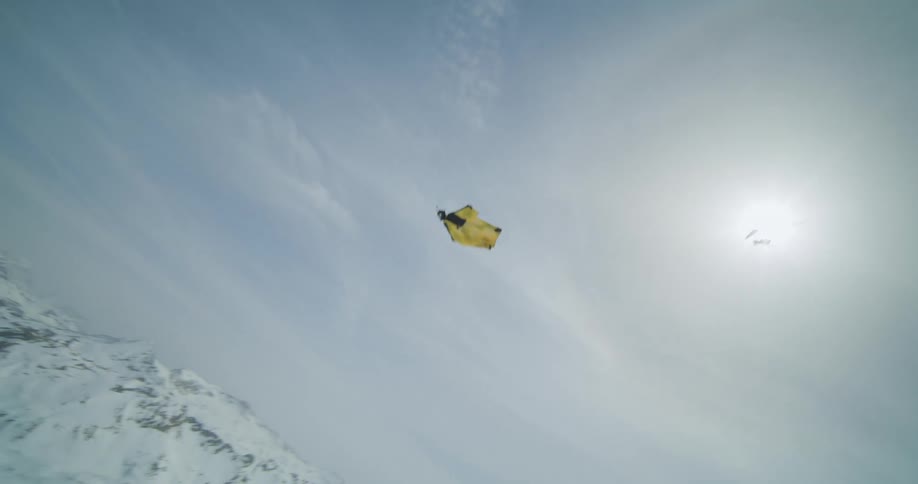 A person jumping from a small yellow plane and gliding down through snowy mountains
