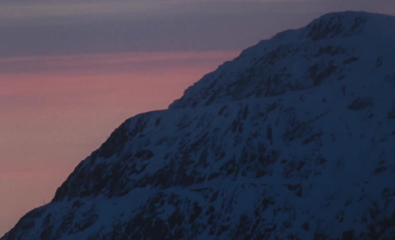 Snow covered mountain stands under a red sky