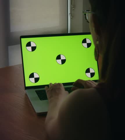 Woman sitting at a desk typing on the keyboard of a laptop with a replaceable green screen