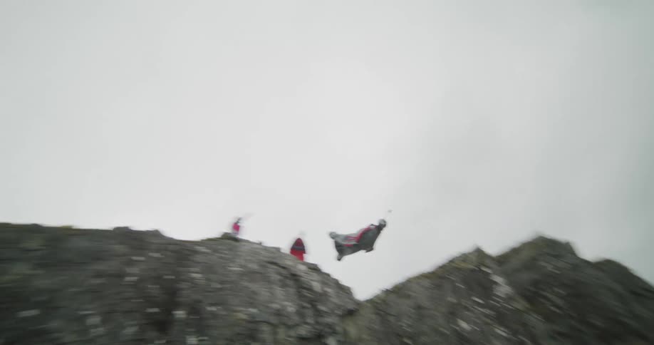 Person wearing wing gliding suit jumps off cliff above ice filled ravine