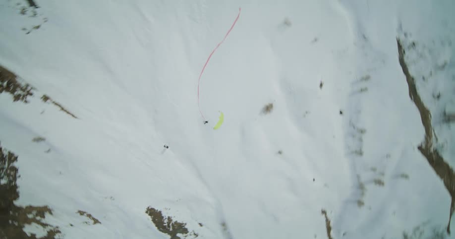 Paraglider flies over snowy terrain while trading a long red ribbon