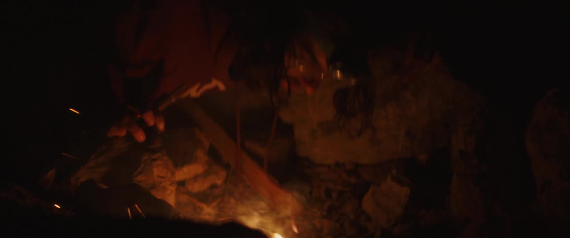 A man blowing on a campfire in darkness