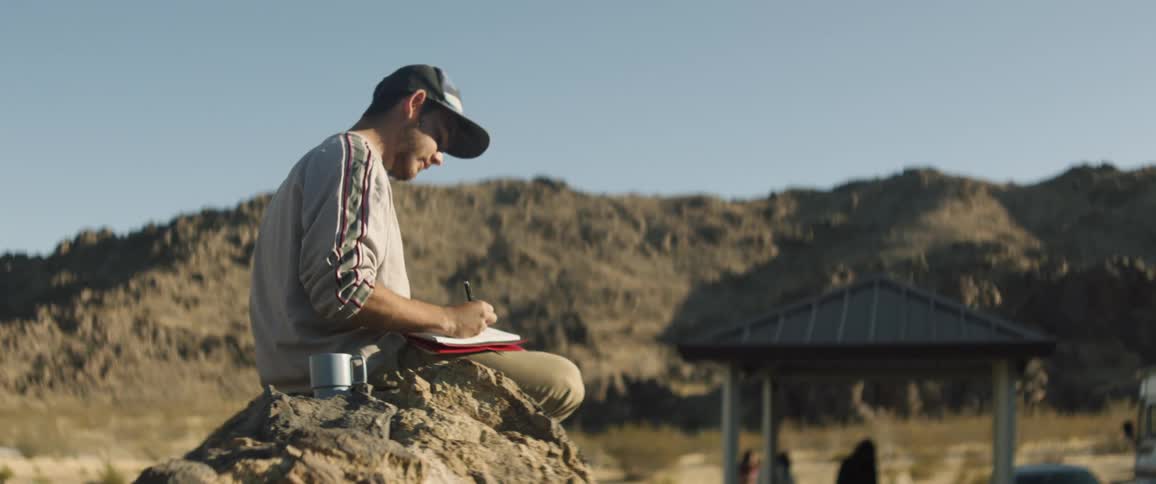 A man journals in his notebook at a campsite in the desert