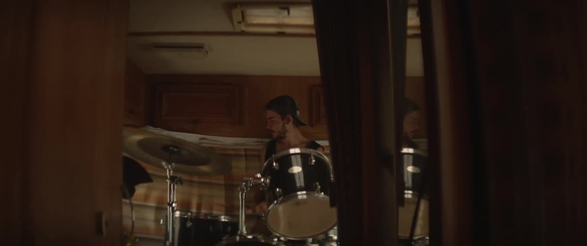 A man in a backwards baseball cap playing drums indoors