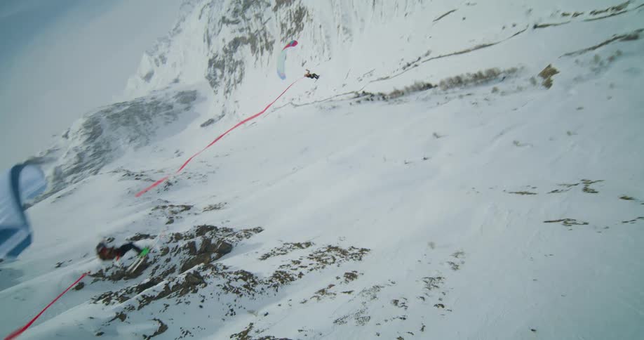 People wearing parachutes fly over a snow covered mountain