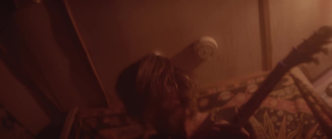 Man with long hair and shirt plays electric guitar in room