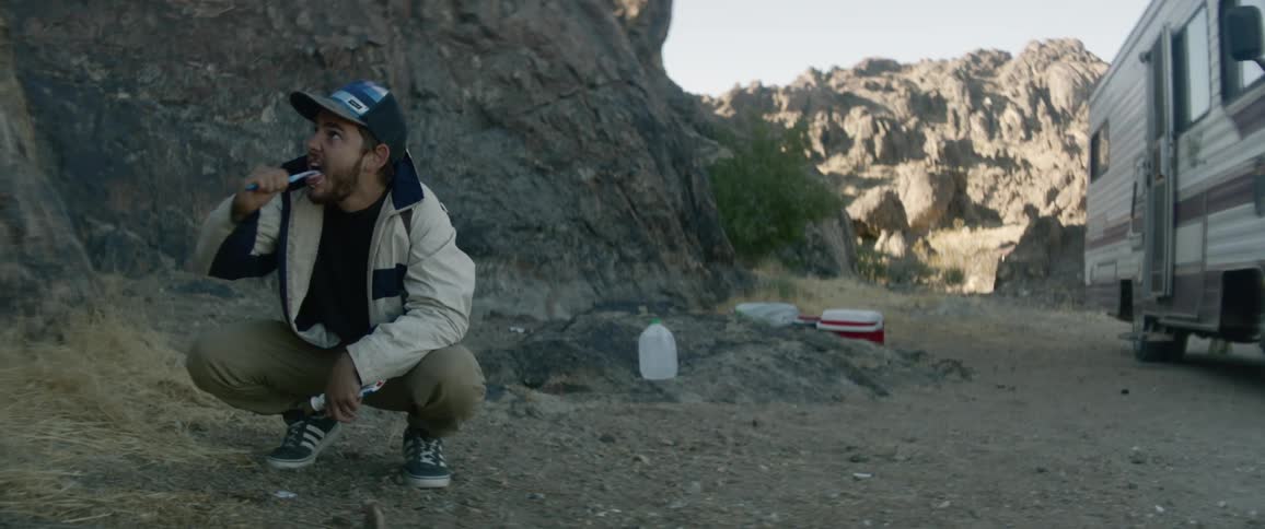 A man brushes his teeth outside his camper while parked in a canyon