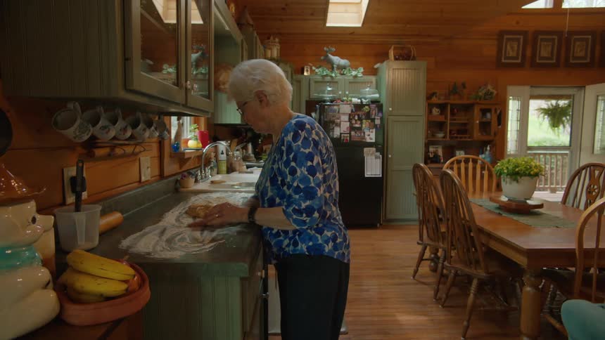 An elderly woman making dough on a kitchen counter at home