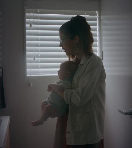 A woman holds a baby facing a bathroom mirror while talking