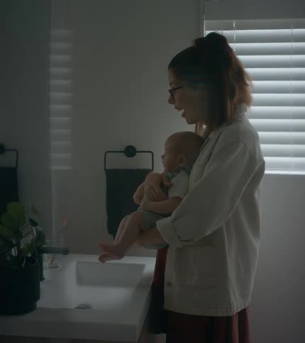 Mother holds baby while pointing at their reflection in bathroom mirror