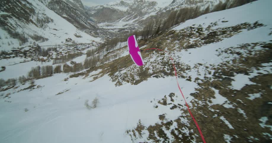 A person wearing skis is paragliding down the side of a snow covered mountain as a long red ribbon follows behind them