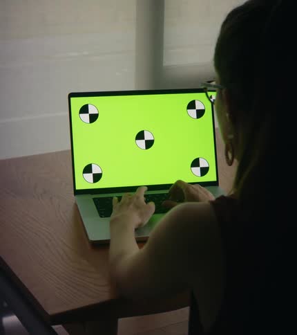 A woman typing on a laptop while sitting at a wood table